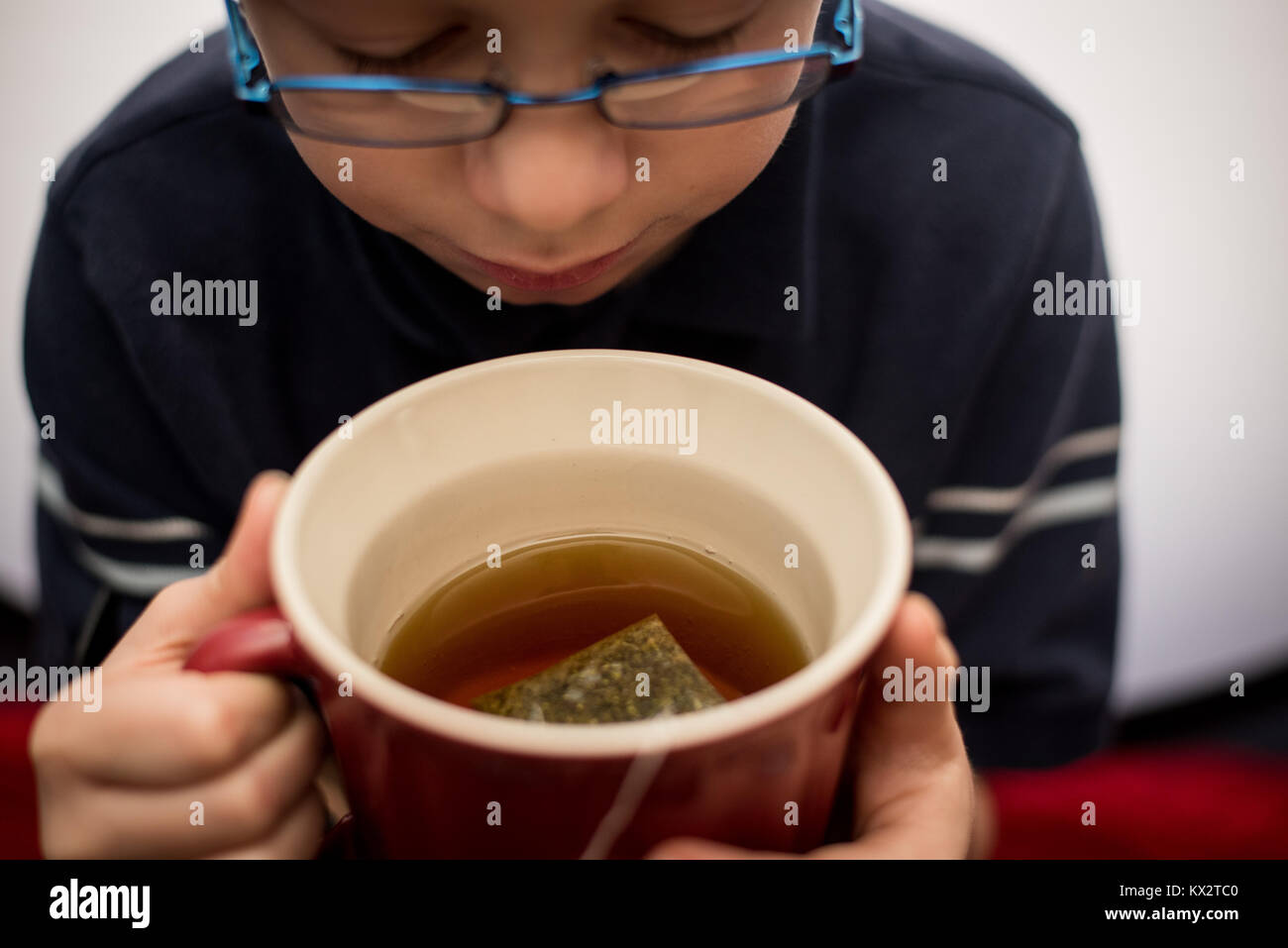 A young boy drinks from a cup of tea in a red cup. Stock Photo