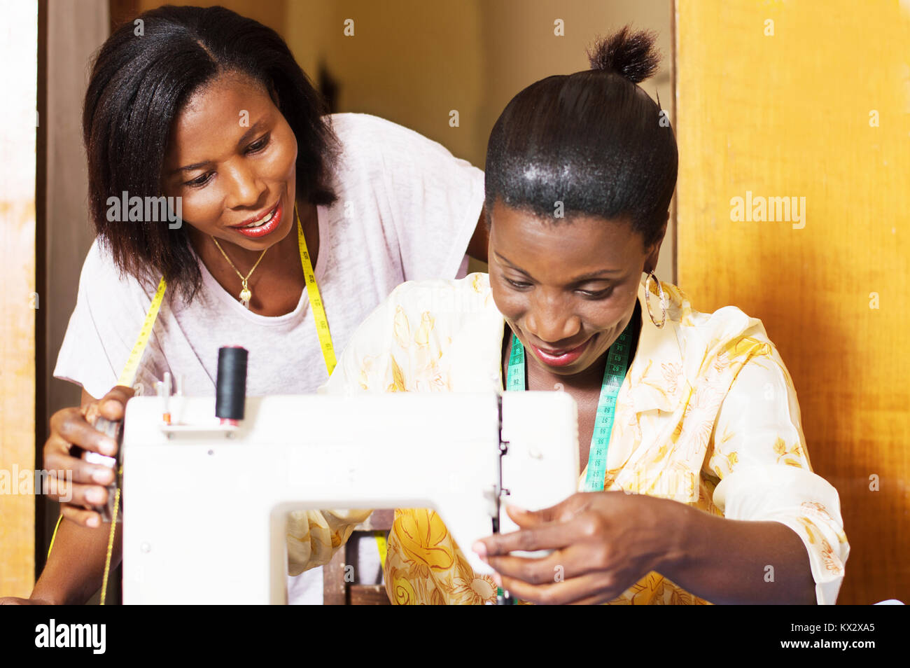 The professional seamstress sews and his trainee assists from behind. Stock Photo