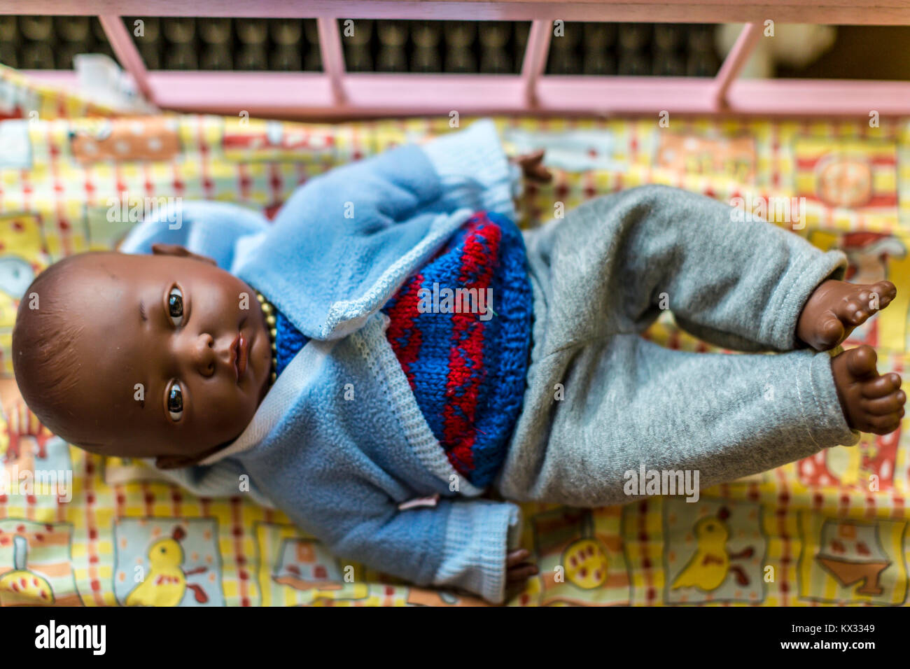 Baby doll with dark skin dressed in blue knitted clothing laying in bed Stock Photo