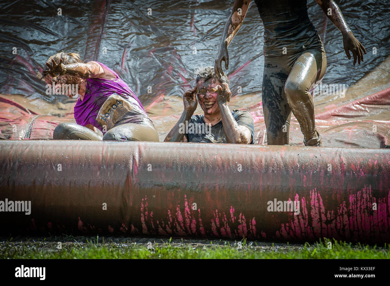 A lady puts her mud covered glasses back on sat in a muddy inflatable during Pretty Muddy 5k Race for Life charity fun run at Windsor Racecourse 2017 Stock Photo