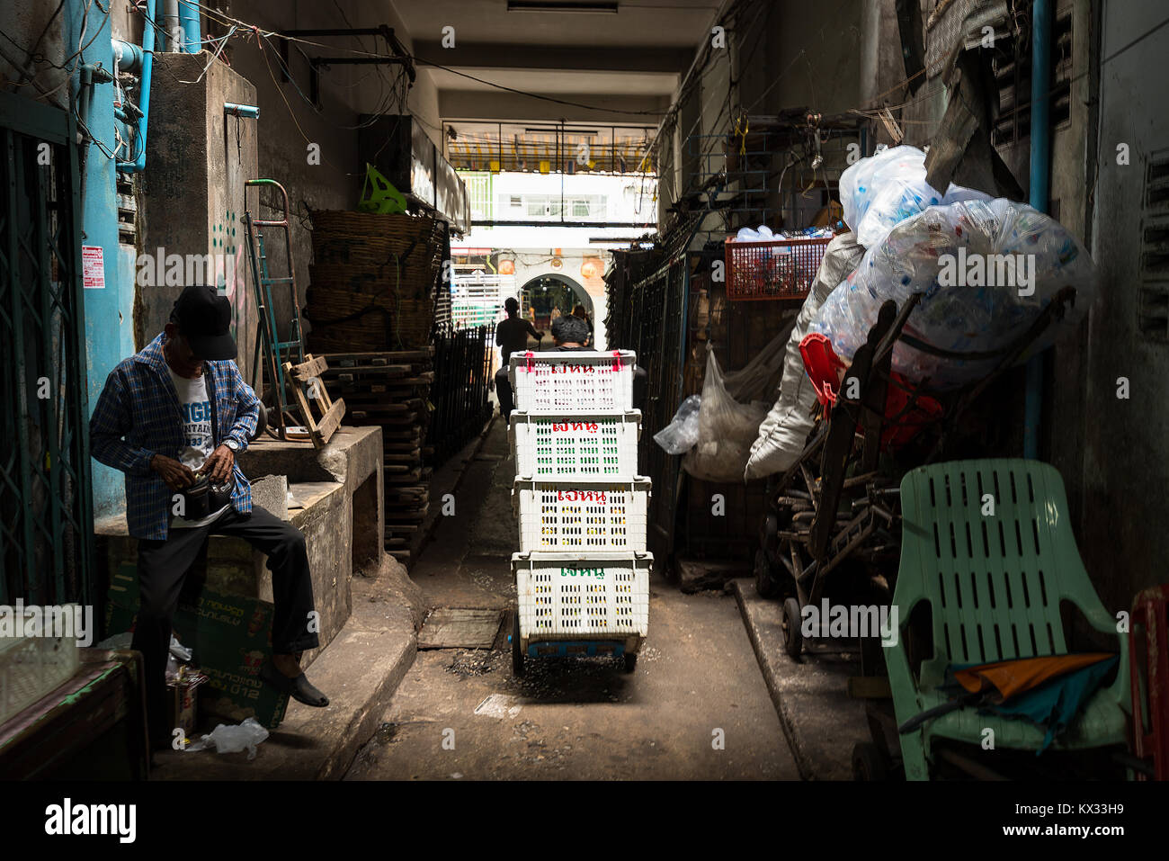 A potter moves plastic crates on a sack truck though a back alley of a wholesale market in Bangkok, Thailand. Stock Photo