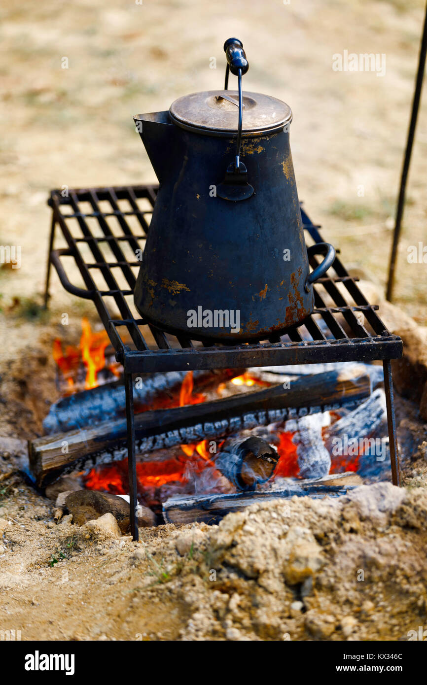 Metal tea kettle heating up over a campfire stock photo - OFFSET