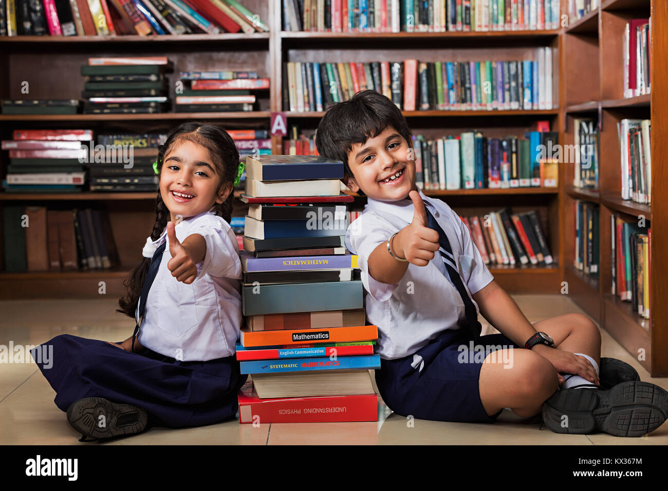 2 Indian School Students Showing Thumbs up With Books In Library Stock Photo