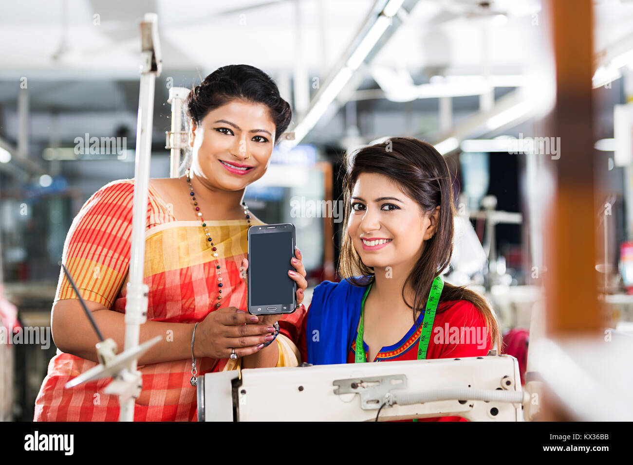 2 Women Workers Colleague Tailor s Reading Text- Message SMS Phone Sewing -Factory Stock Photo