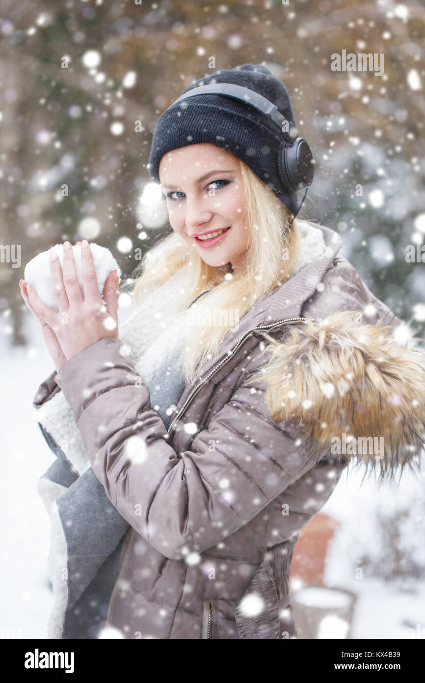 Young blonde woman making snowball and listening music in snowfall, winter portrait Stock Photo