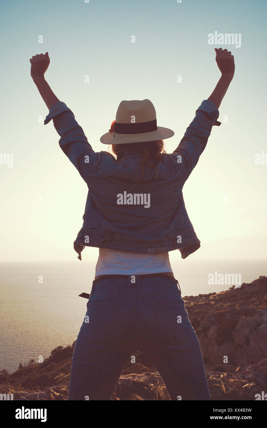 Young carefree woman in hat hands up in the air on cliff vintage Stock Photo