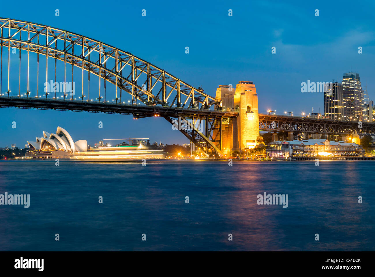 Night panorama of Sydney Harbour, Australia. Cityscape at night, Sydney Harbour Bridge, ferry passes in front of Opera House. Stock Photo