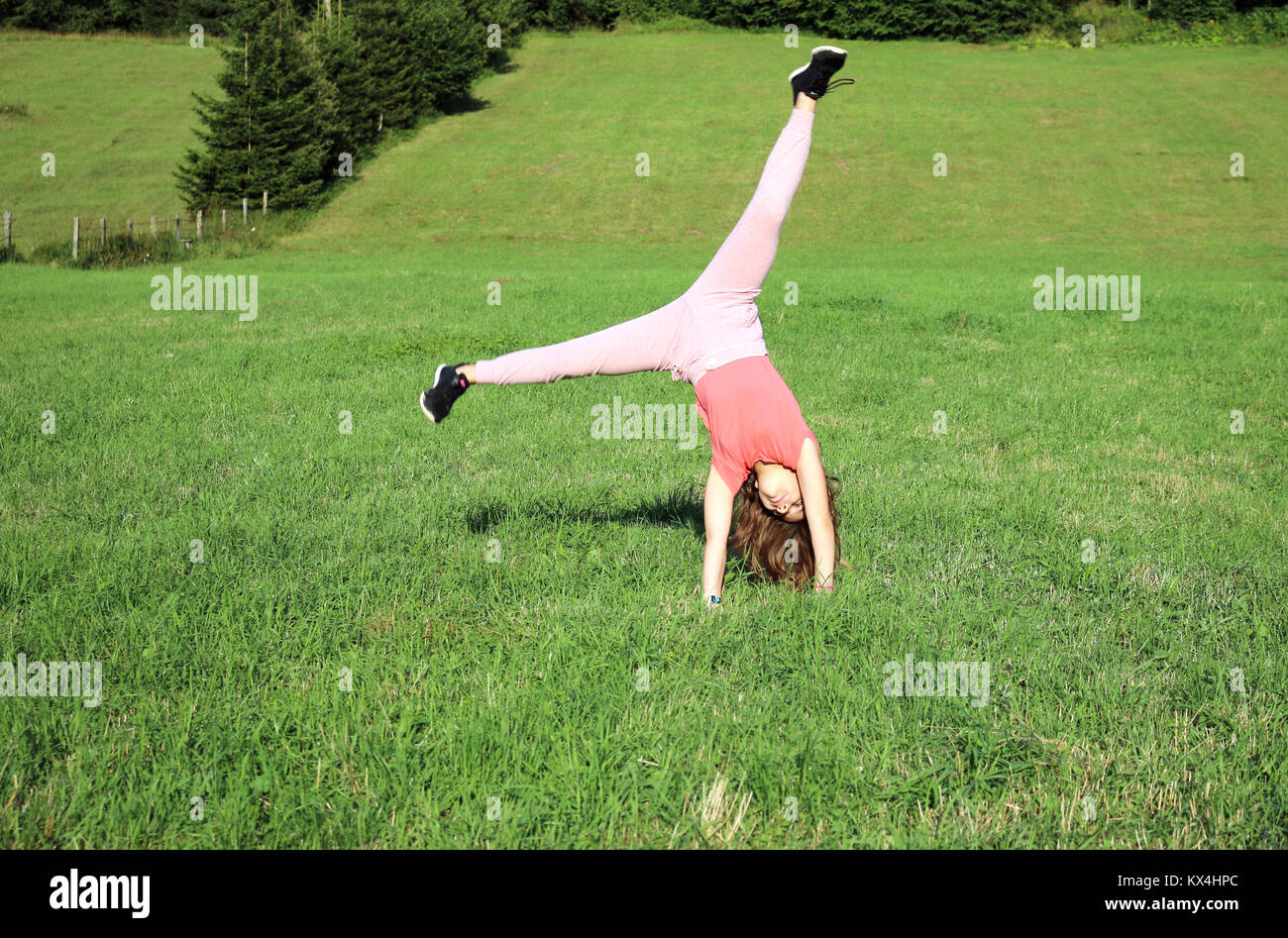 happy little girl doing catwheel on green field Stock Photo