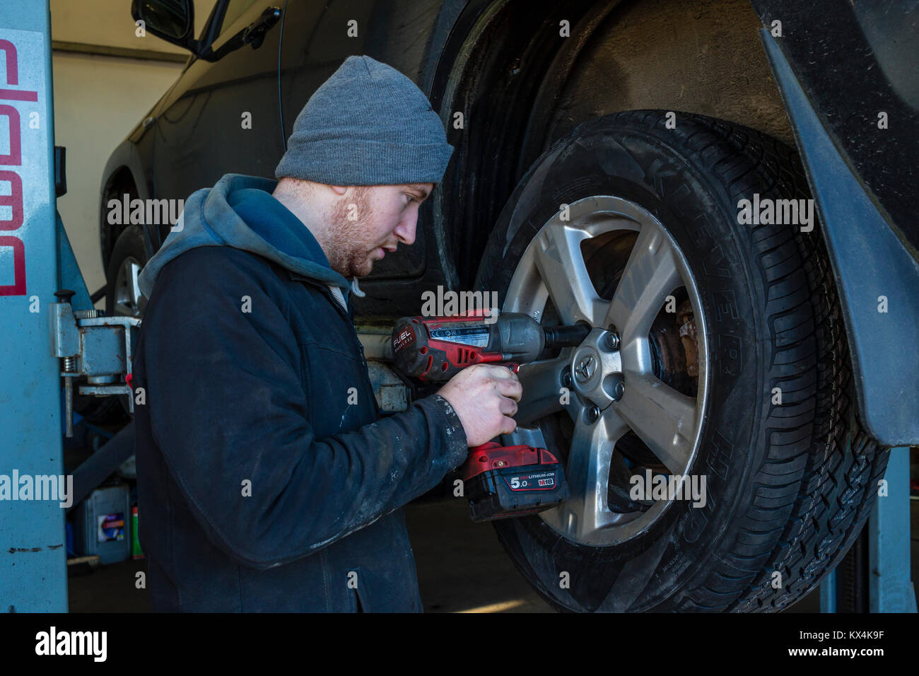 Young Apprentice mechanic removing a car wheel with a cordless impact wrench Stock Photo