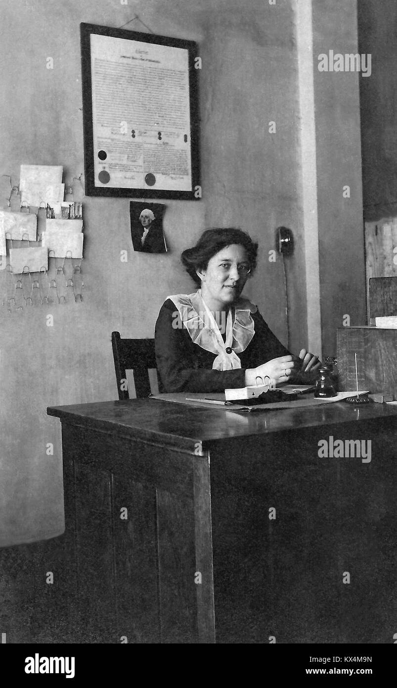 Historical photo of a woman seated at a small wooden office desk, circa 1910. Stock Photo