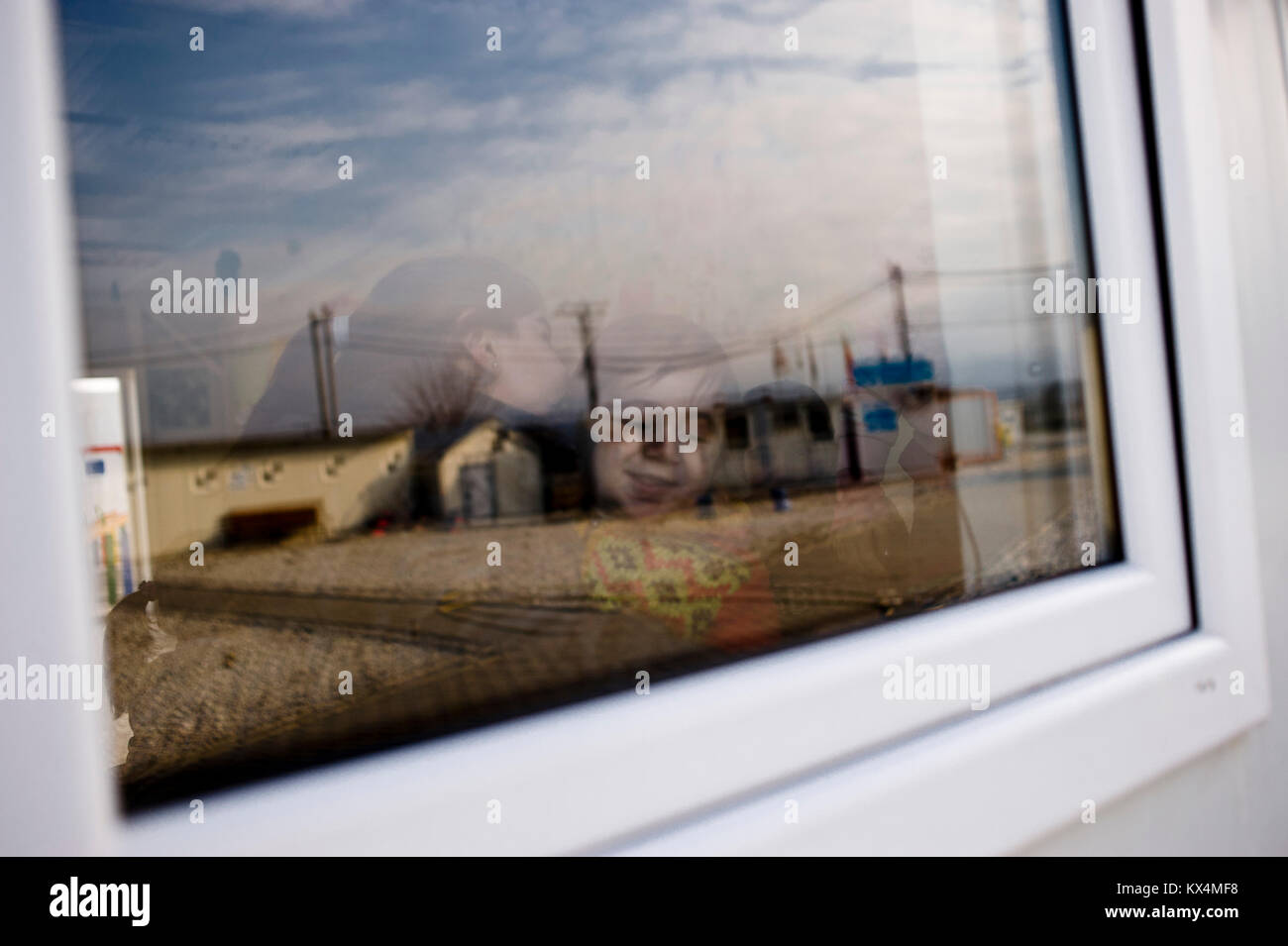 A refugee child is seen through the window of a container house in the arms of a caregiver at the Vinojug Temporary Transit Center in Gevgelija, south Stock Photo