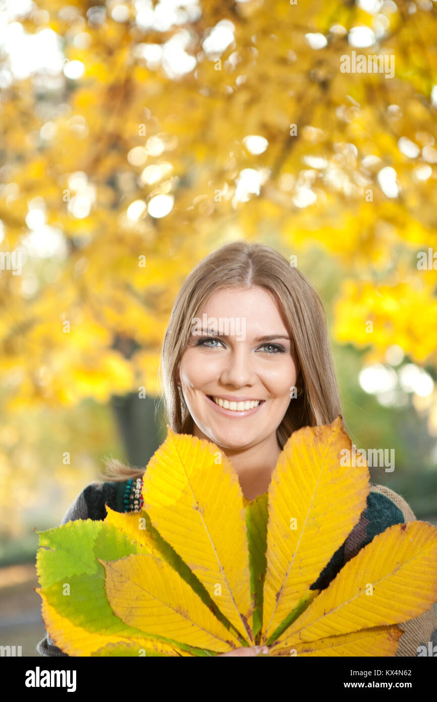 smiling young girl holding big yellow leaf in front her Stock Photo - Alamy