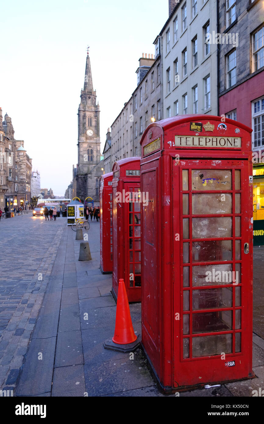 Row of red telephone boxes along cobbled High Street with tower in background and evening light following sunset Old Town, Edinburgh, Scotland Stock Photo