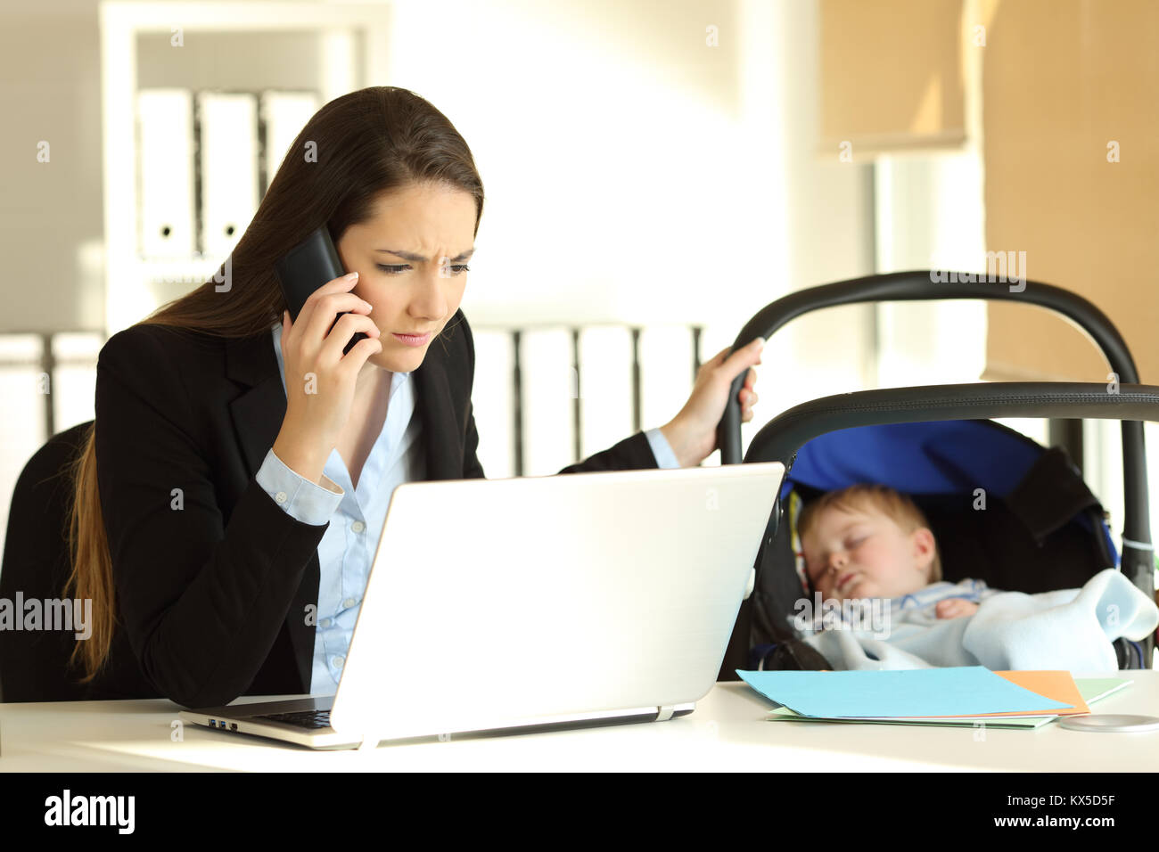 Stressed mother working attending a phone call and taking care of her baby at office Stock Photo