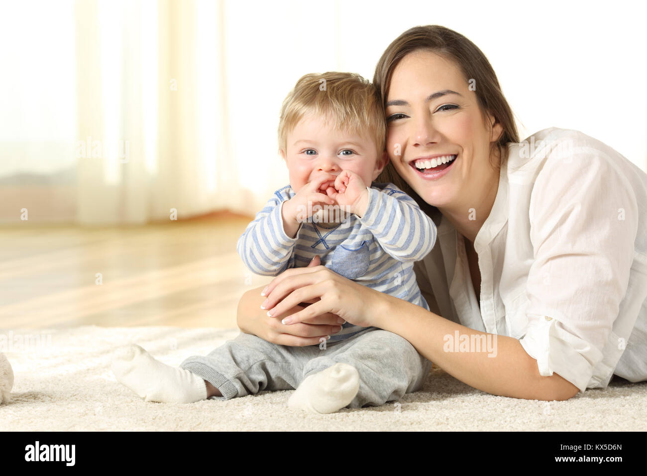 Smiley mother and her baby looking at you lying on the floor at home Stock Photo