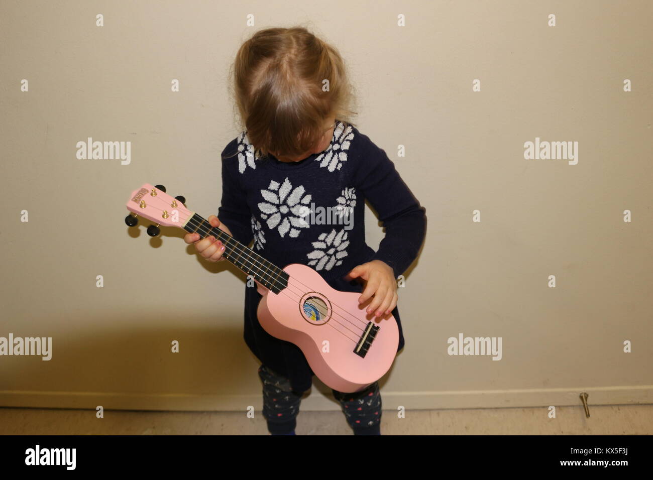 A young caucasian girl with blonde hair is learning to play the ukulele