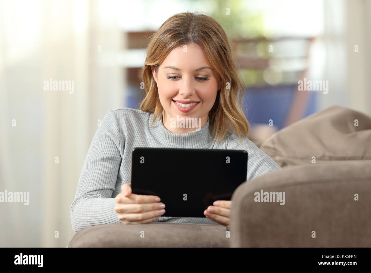 Front view of a woman watching video in a tablet sitting on a couch in the living room at home Stock Photo