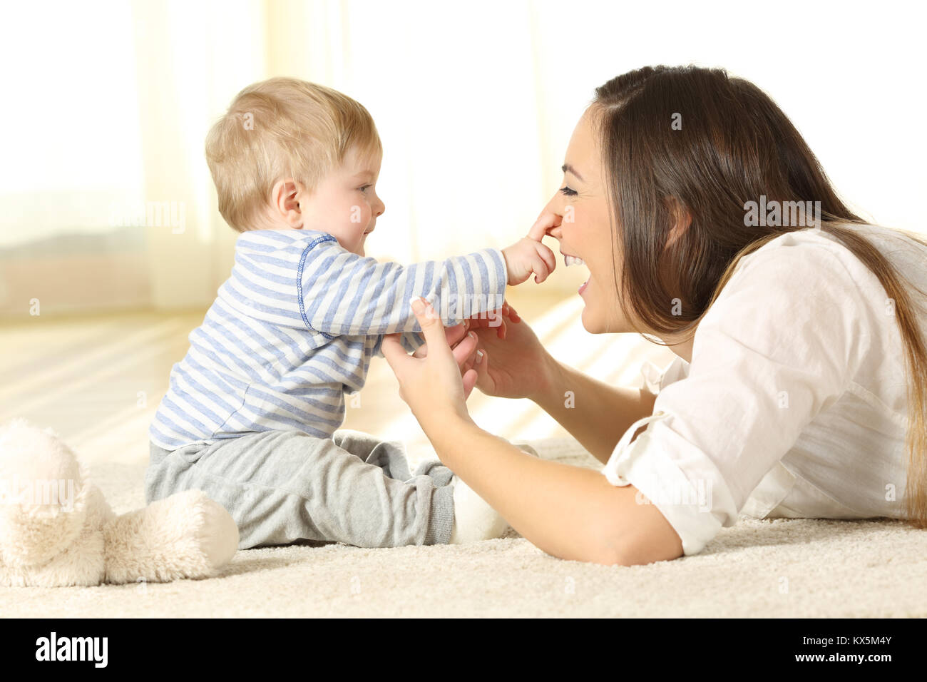 Happy baby touching his mother face lying on a carpet at home Stock Photo
