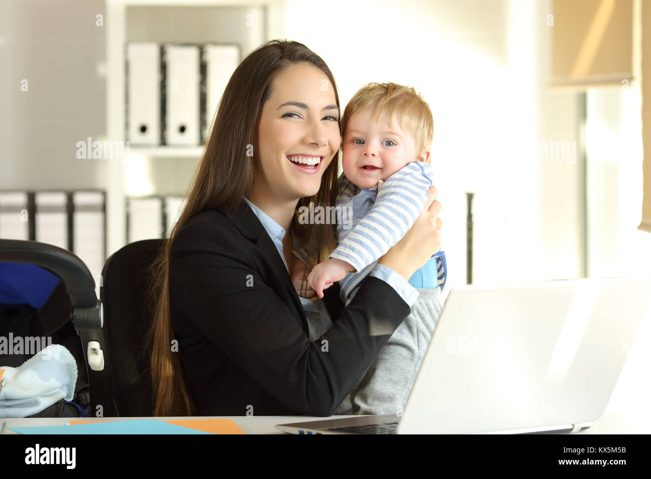 Portrait of a happy working mother posing with her baby and looking at camera at office Stock Photo