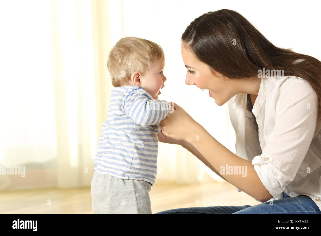 Proud mother helping her baby son in his first steps at home Stock Photo