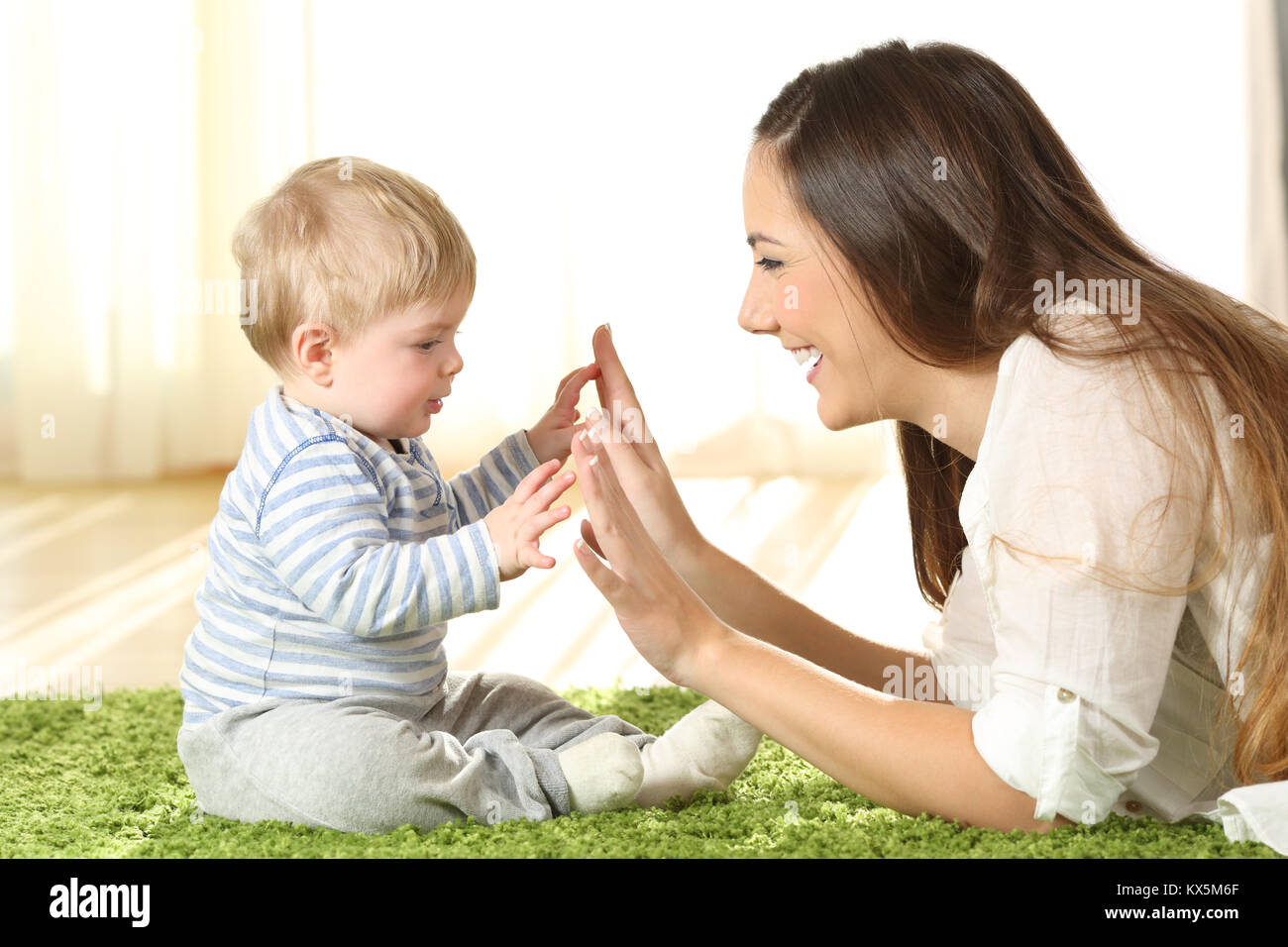 Side view portrait of a happy mother playing with her baby touching hands on a carpet at home Stock Photo