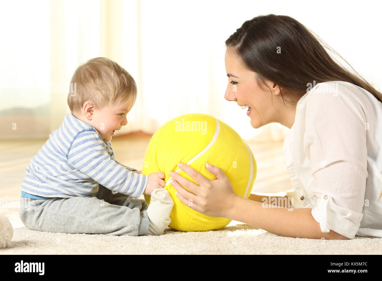 Side view portrait of a happy mother playing with her baby with a ball lying on the floor at home Stock Photo