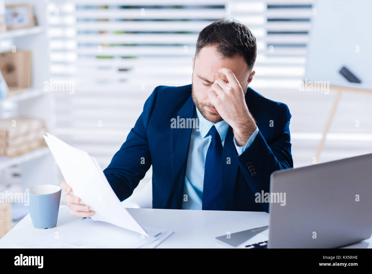 Exhausted worker sitting with his eyes closed and holding documents Stock Photo