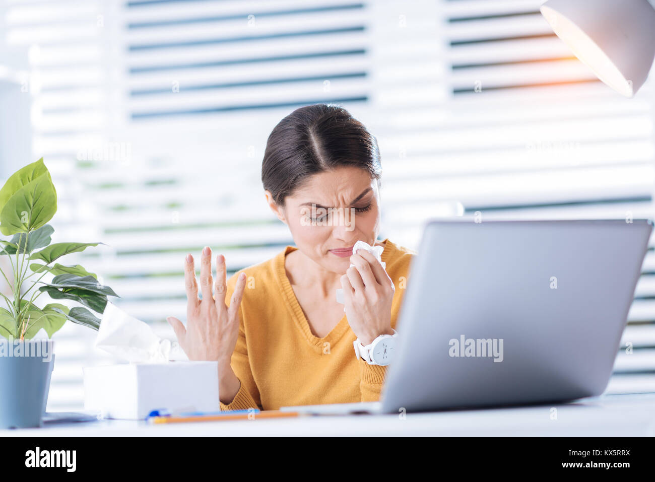 Upset ill woman having a running nose and trying to work in the office Stock Photo