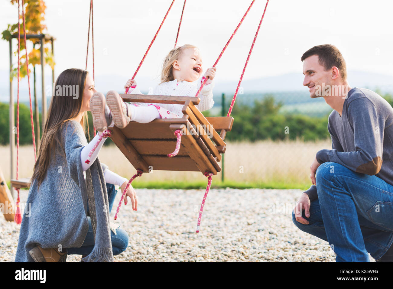 Family With Little Girl Swinging On A Playground Childhood