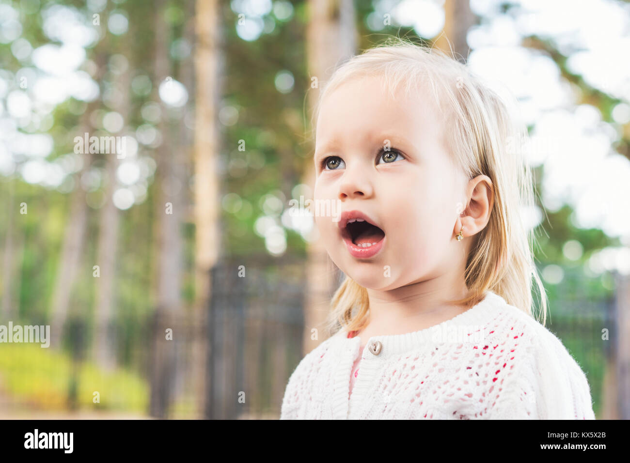 Image of sweet baby girl looking away from camera with mouth open in amazement. Close up portrait of a child. Cute toddler with green eyes portrait. Stock Photo