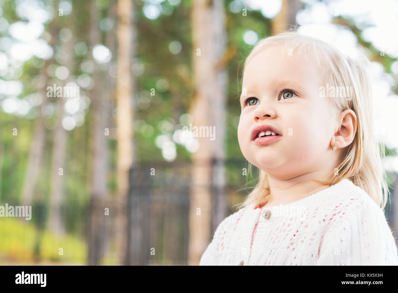 Image of sweet overweight baby girl looking away from camera. Close up portrait of a child. Cute toddler with green eyes outdoor portrait. Stock Photo