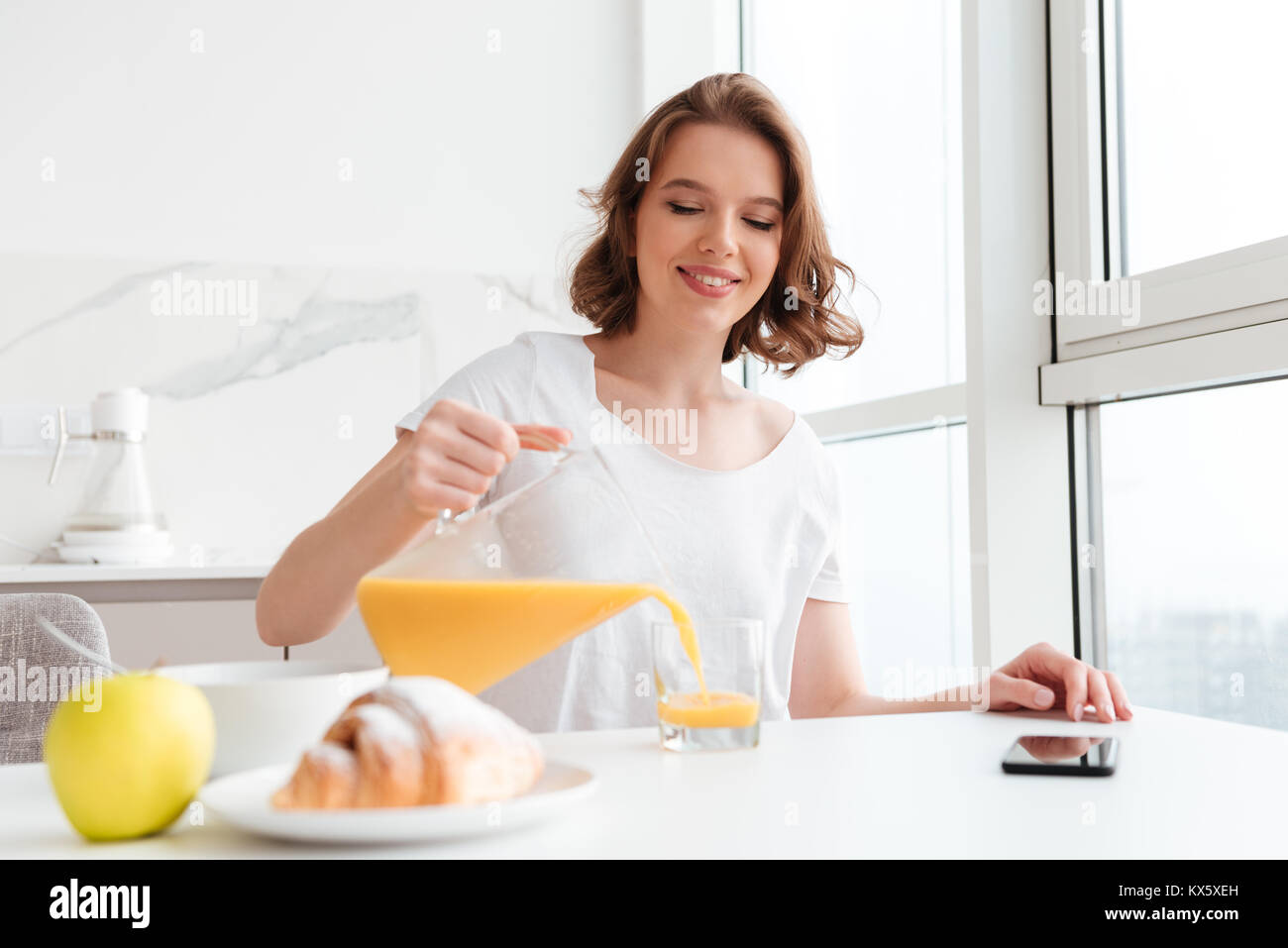 Cheerful girl pouring juice into glass while sitting and