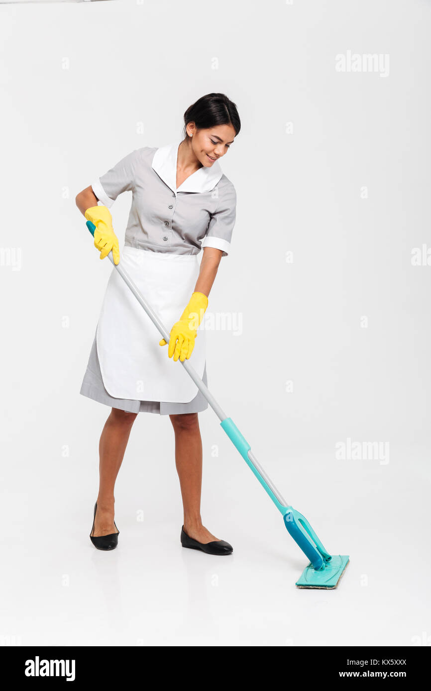 Full length portrait of young attractive woman in uniform cleaning floor with mop, isolated over white background Stock Photo