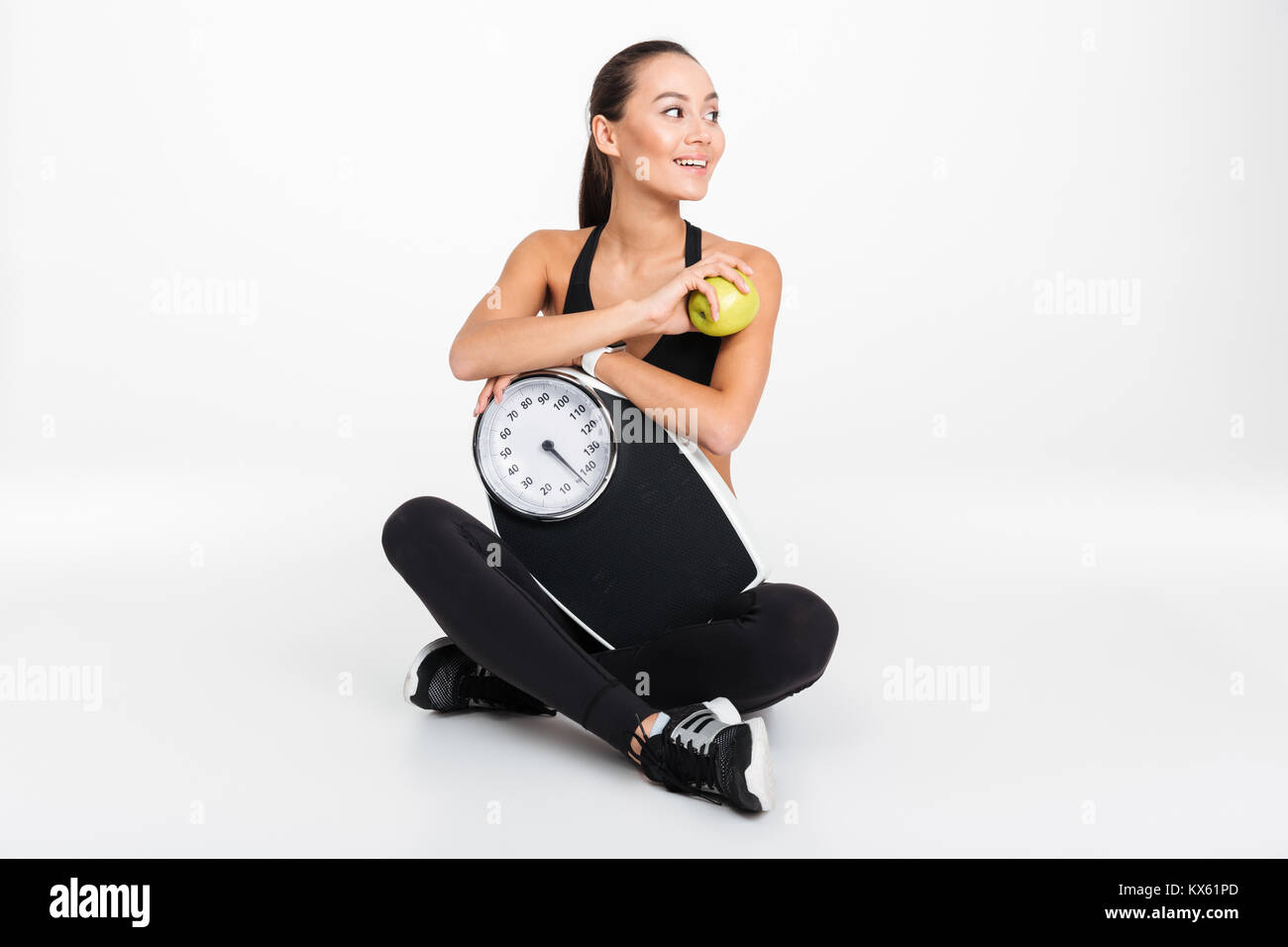 Portrait of a cheerful asian fitness woman holding weight scales and an ...