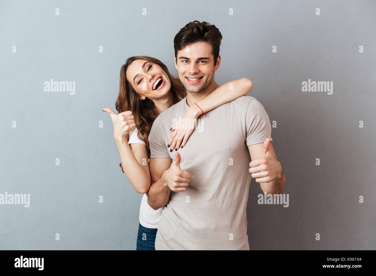 Portrait of a happy young couple hugging while standing and showing ...
