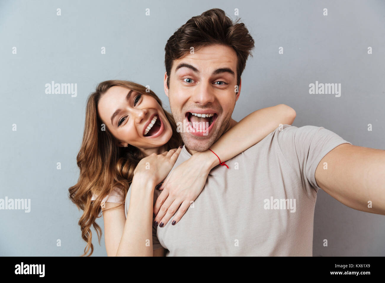 Portrait of an excited young couple hugging while standing and taking a ...