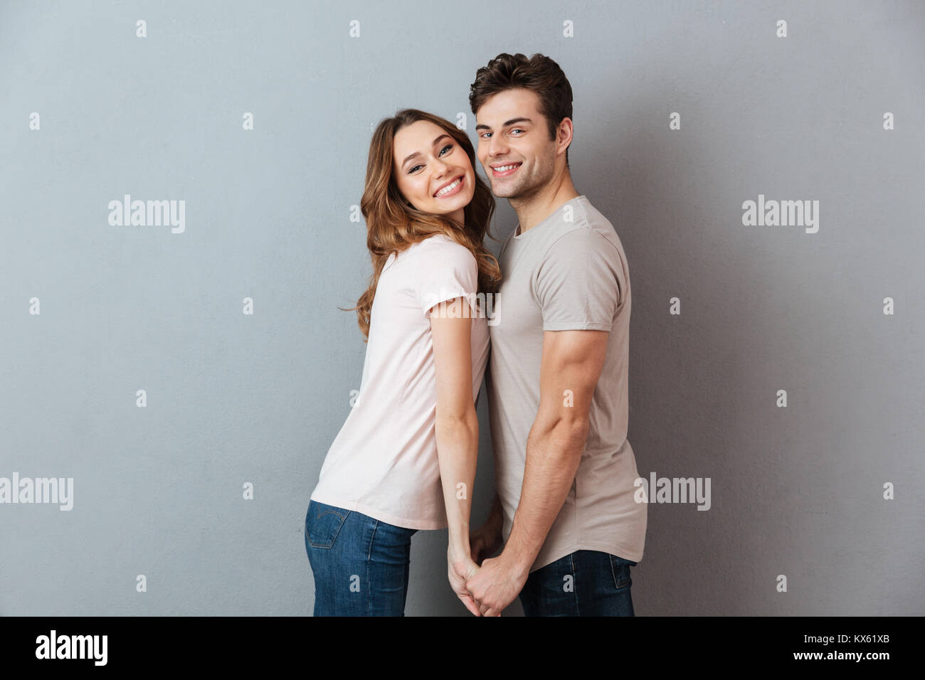 Portrait of a happy young couple holding hands and looking at camera ...