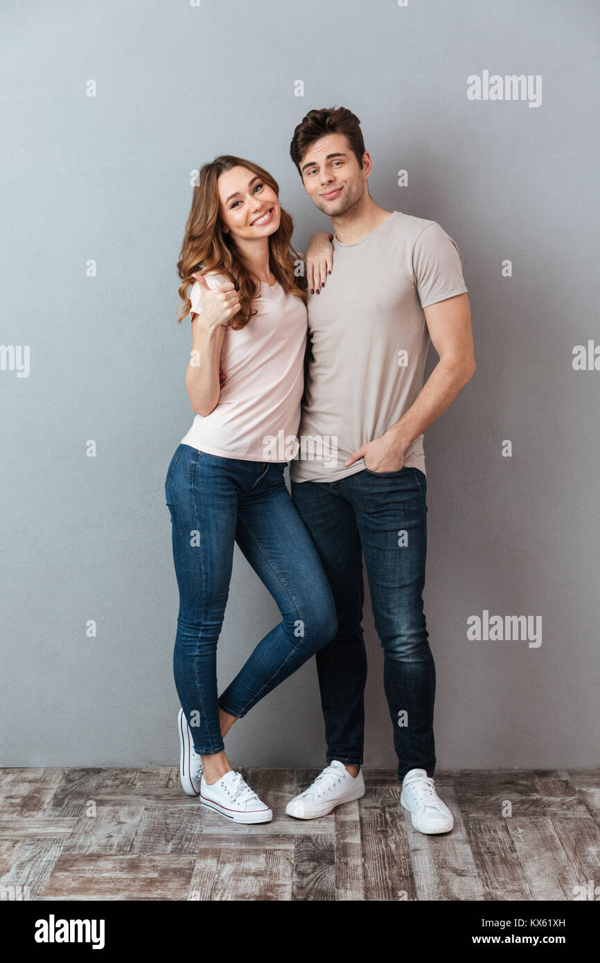 Full length portrait of a happy smiling couple hugging and showing ...