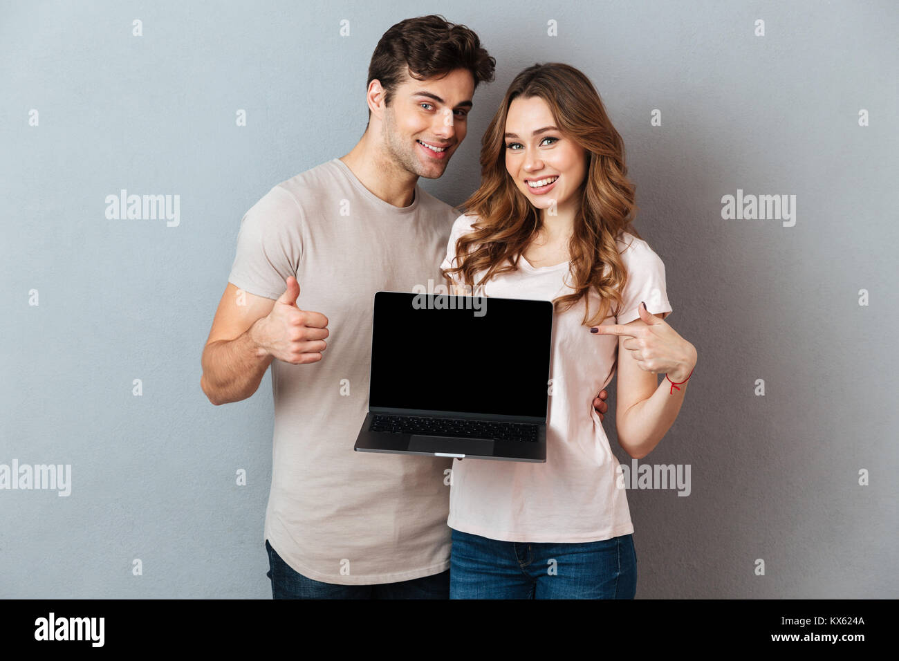 Portrait of a smiling happy couple pointing at blank screen laptop ...