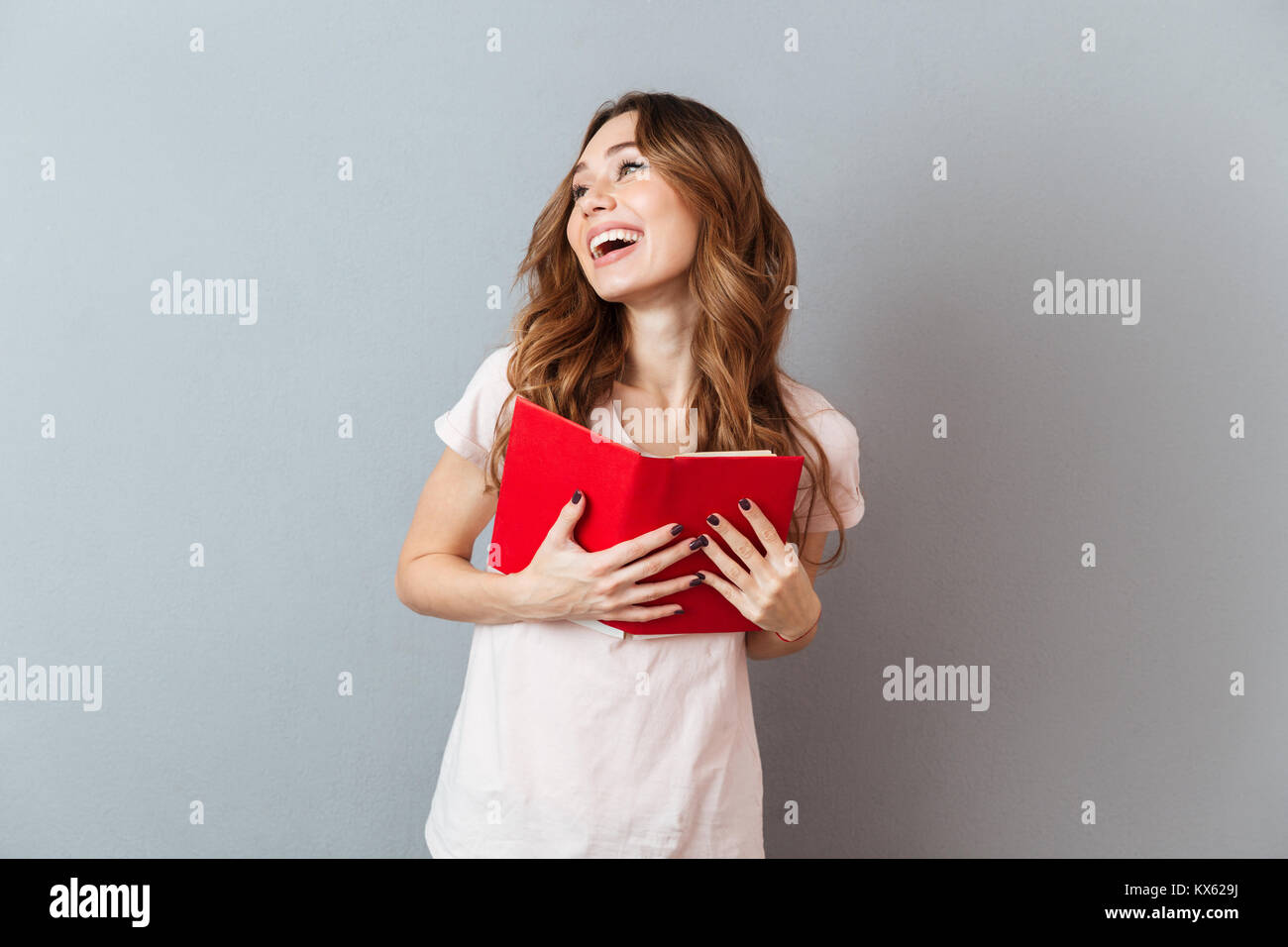 Portrait of a pretty laughing girl holding book and looking away ...