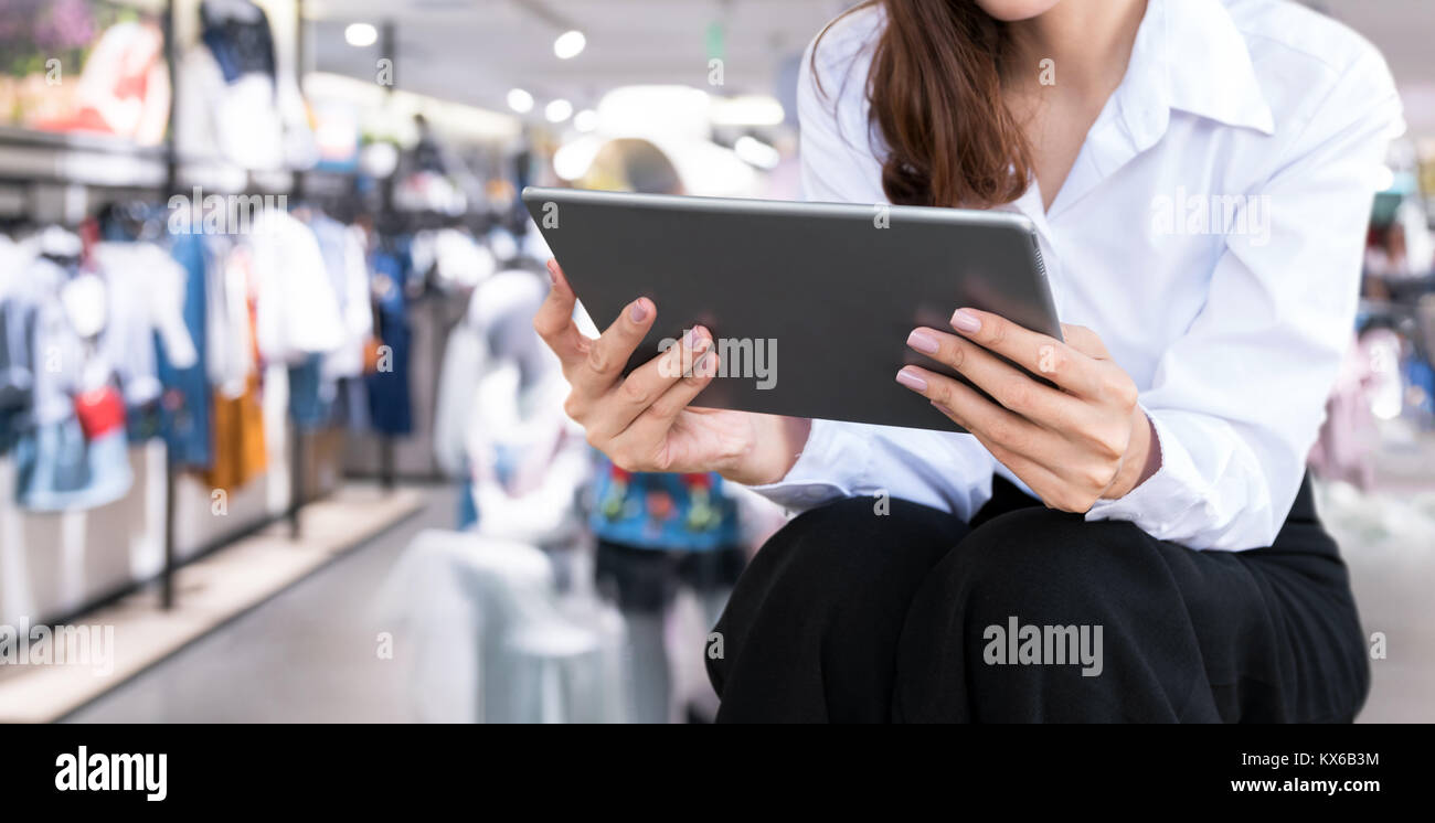 Smart retail internet of things , chatbot , online shopping technology trend concept. Female worker using tablet and blur retail shop background. Stock Photo