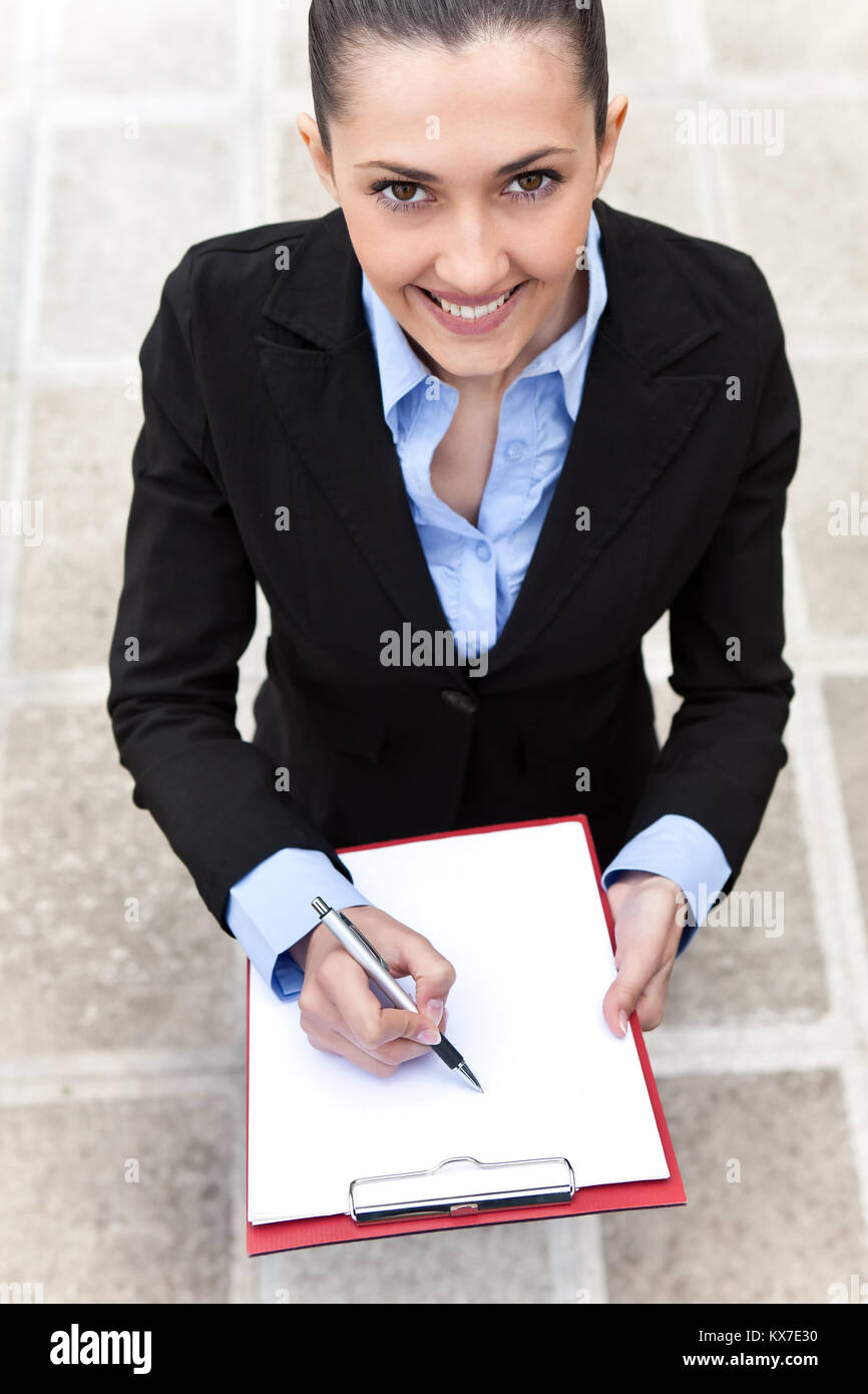 businesswoman standing outdoor and making note, smiling woman looking at camera, top view Stock Photo