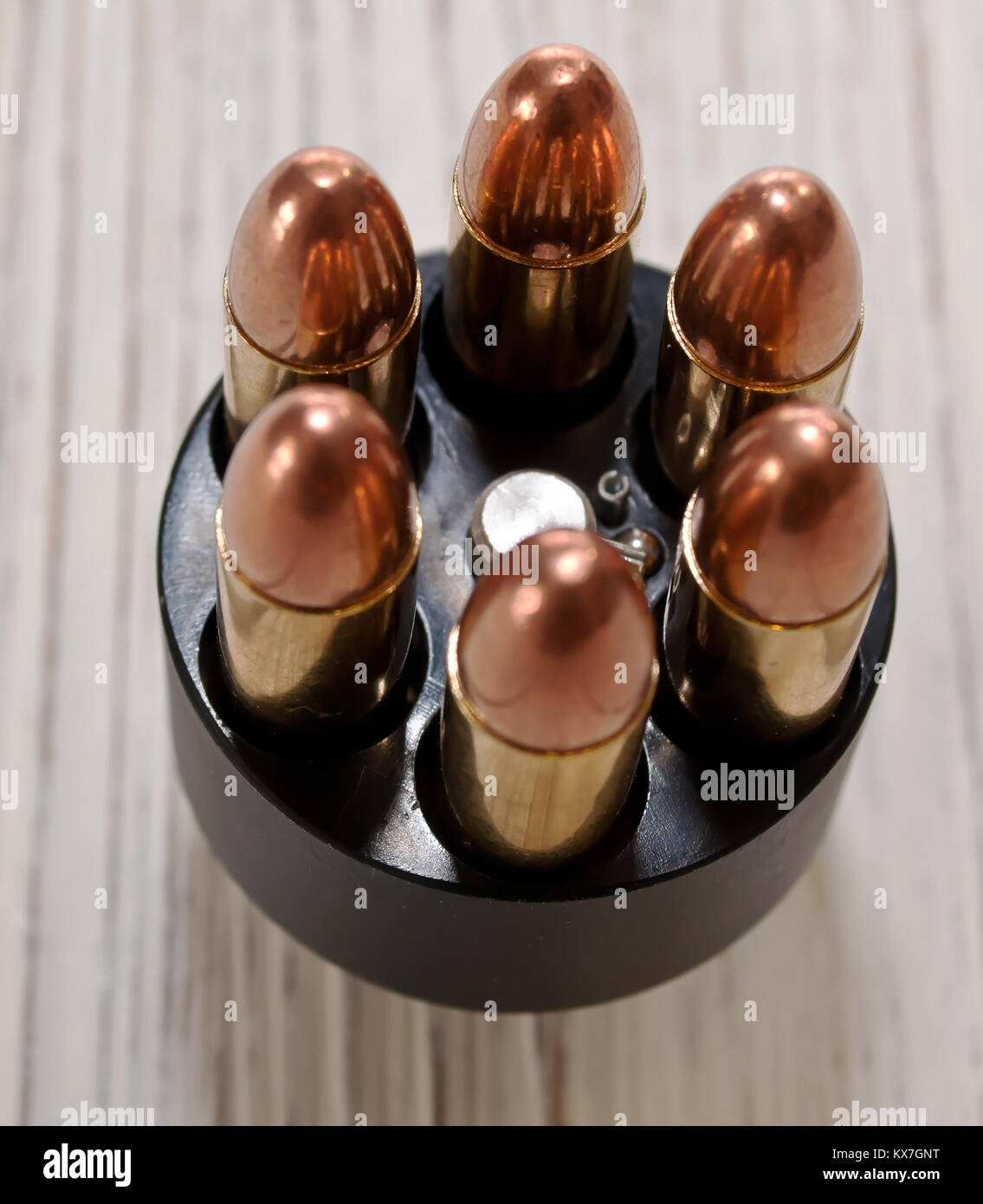 A close up top view of a revolver's speed loader, loaded with six bullets sitting on a white wooden table Stock Photo