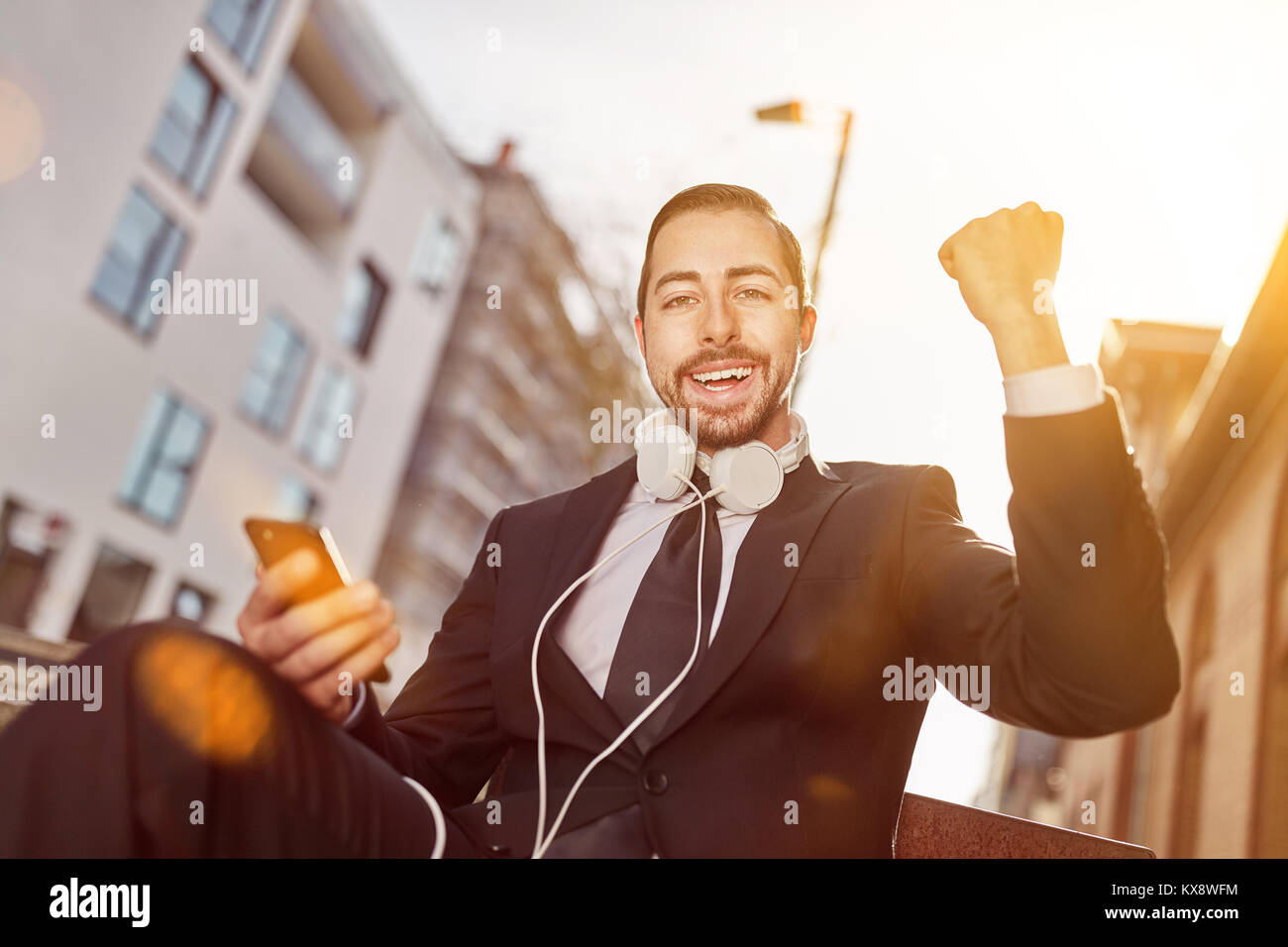 Exulting businessman with smartphone and headphones is clenching the fist Stock Photo