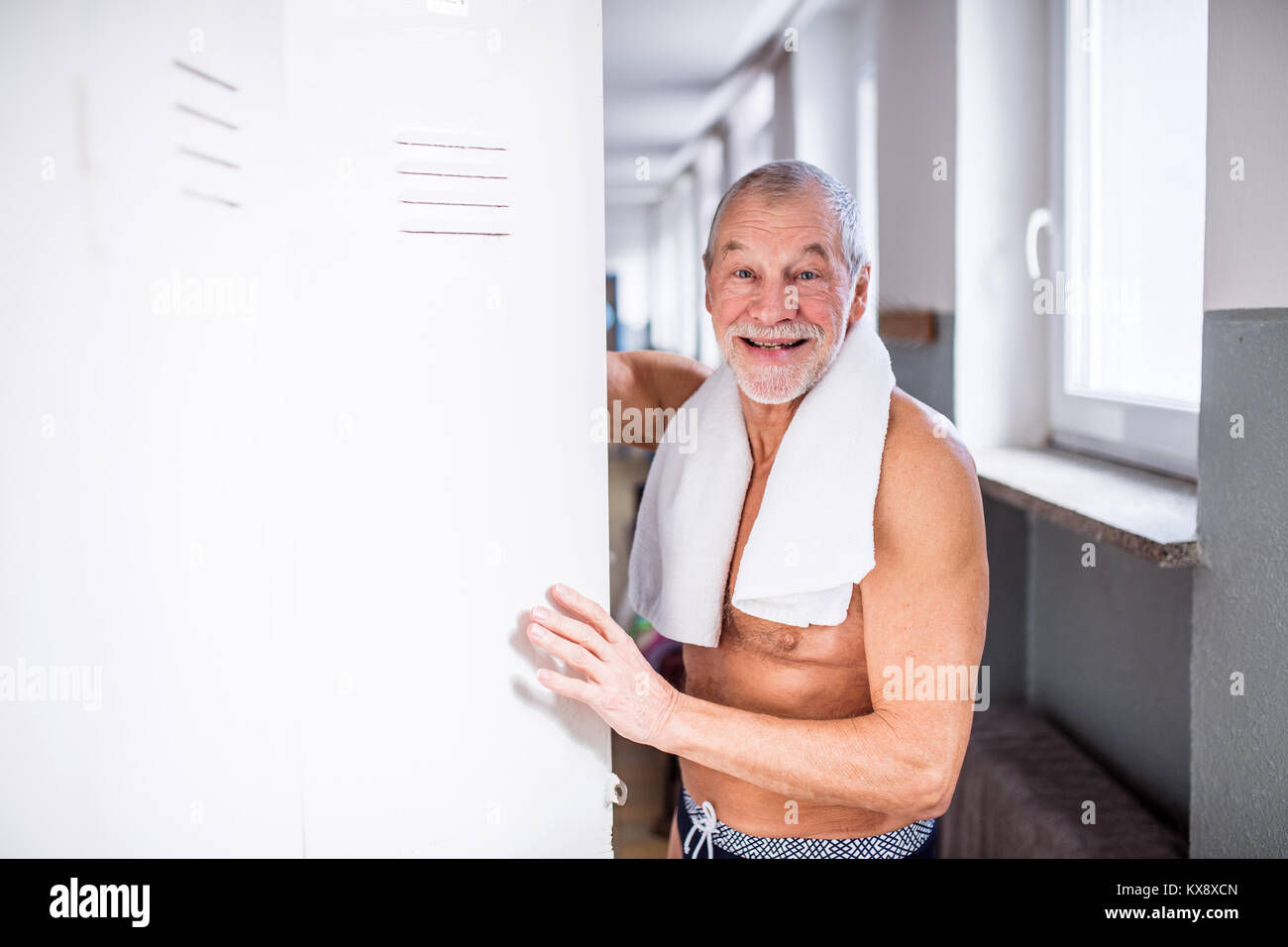 Senior man standing by the lockers in an indoor swimming pool. Stock Photo