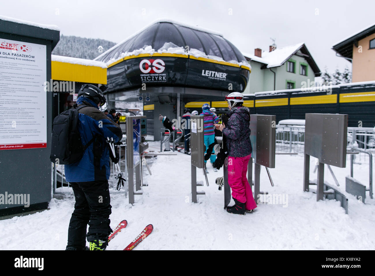 Skiers and Snowboarders going through tripod turnstiles gates and boarding chairlift heading for the summit of Skrzyczne mountain in Szczyrk Poland Stock Photo