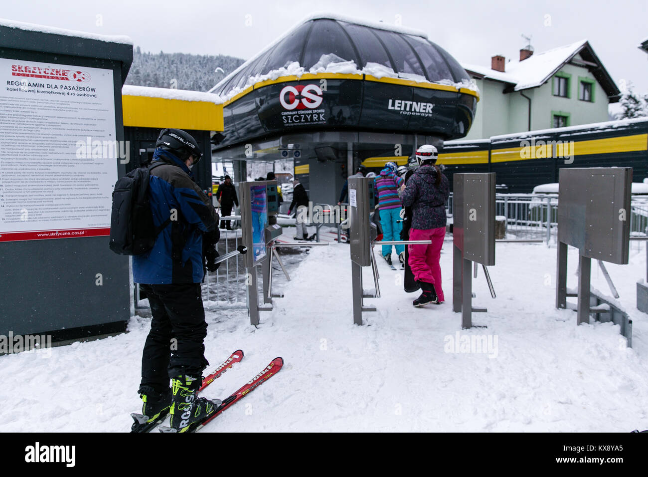 Skiers and Snowboarders going through tripod turnstiles gates and boarding chairlift heading for the summit of Skrzyczne mountain in Szczyrk Poland Stock Photo