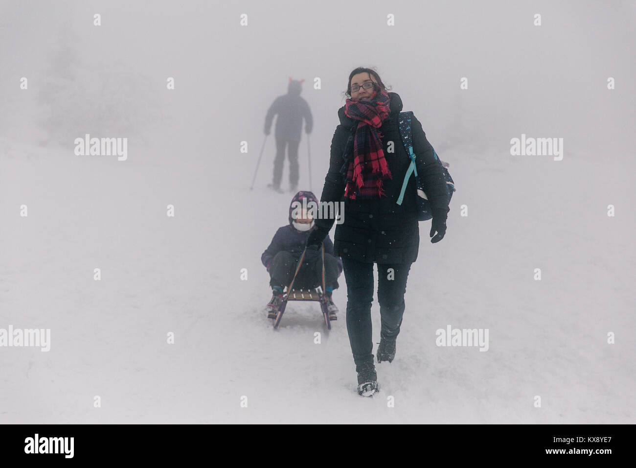 Mum pulling sledge with her daughter at the covered in snow and mist summit of Skrzyczne mountain in Szczyrk Poland Stock Photo