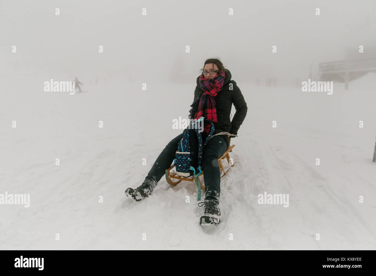 Girl having fun trying to ride on a sledge at the misty and covered in snow summit of Skrzyczne mountain in Poland Stock Photo