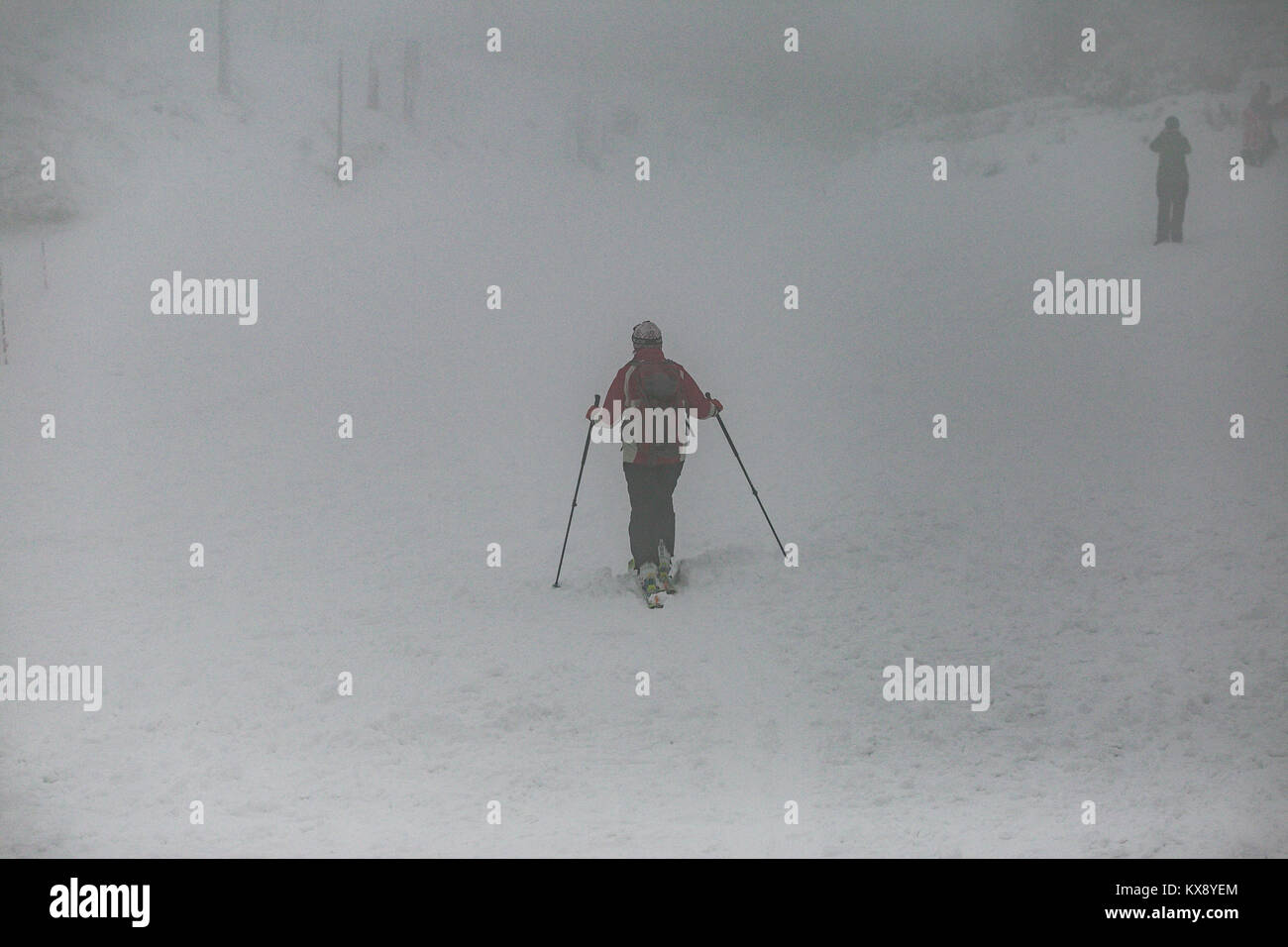 Hiker with trekking poles arriving at covered in snow and mist summit of Skrzyczne mountain in Szczyrk heading for the hiking trails Stock Photo